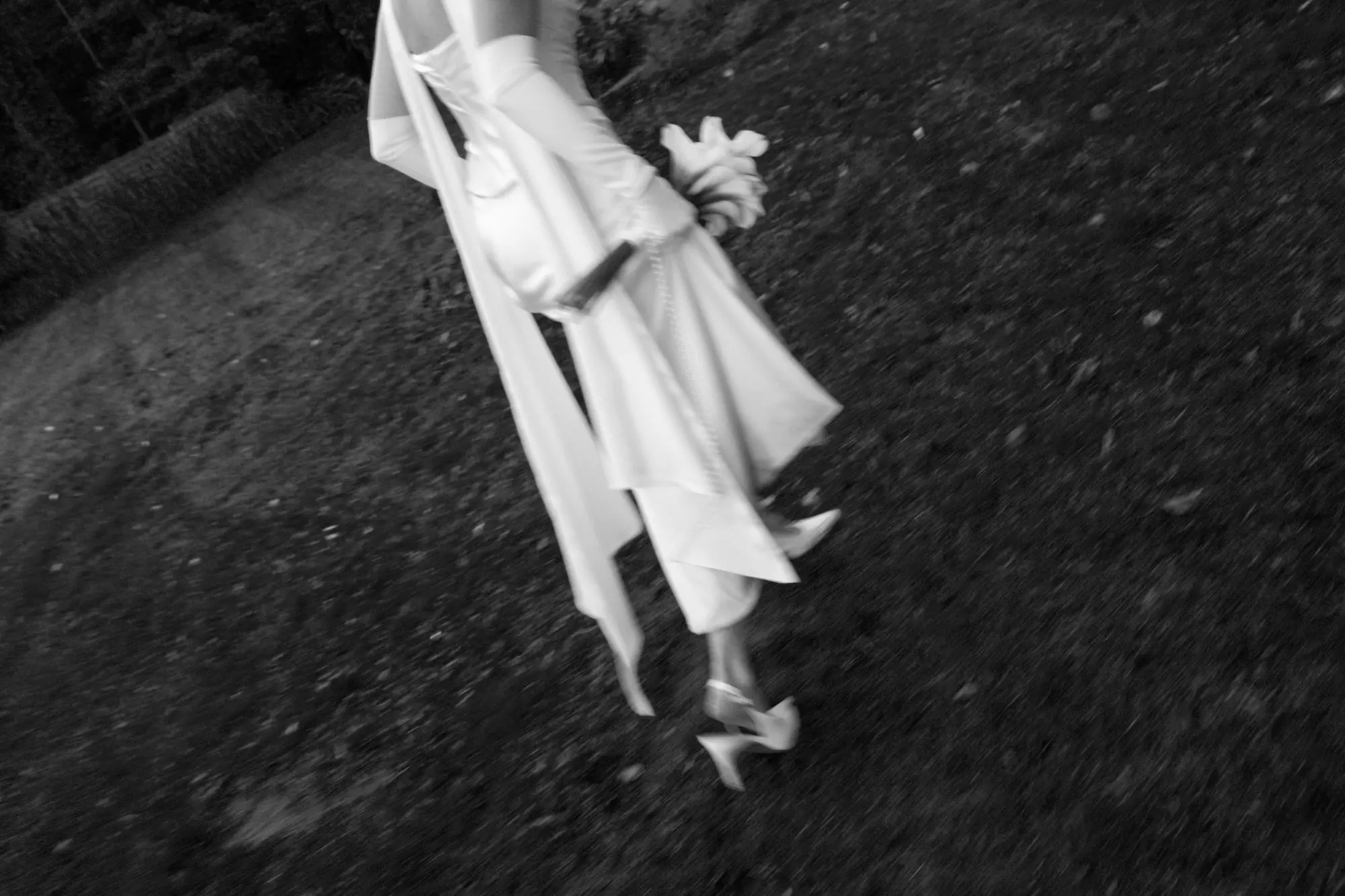 Bride walking across the grass with her bouquet, dress ribbons flowing in the wind