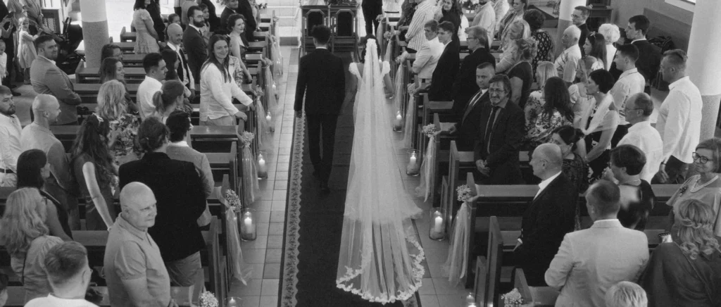Bride and groom walking down the church aisle between full pews, long veil behind
