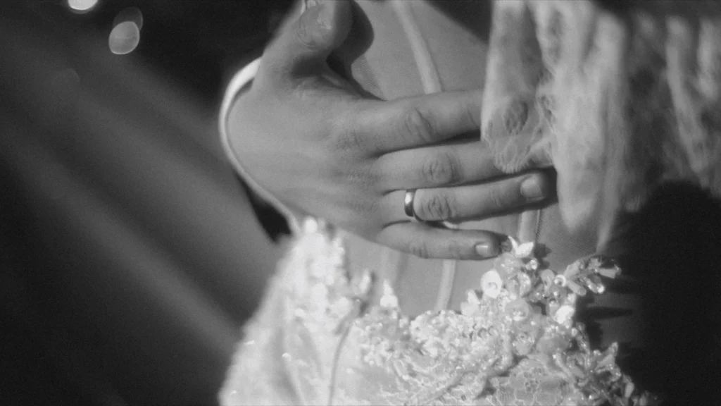 Groom's hand with his wedding ring resting on the bride's beaded lace gown