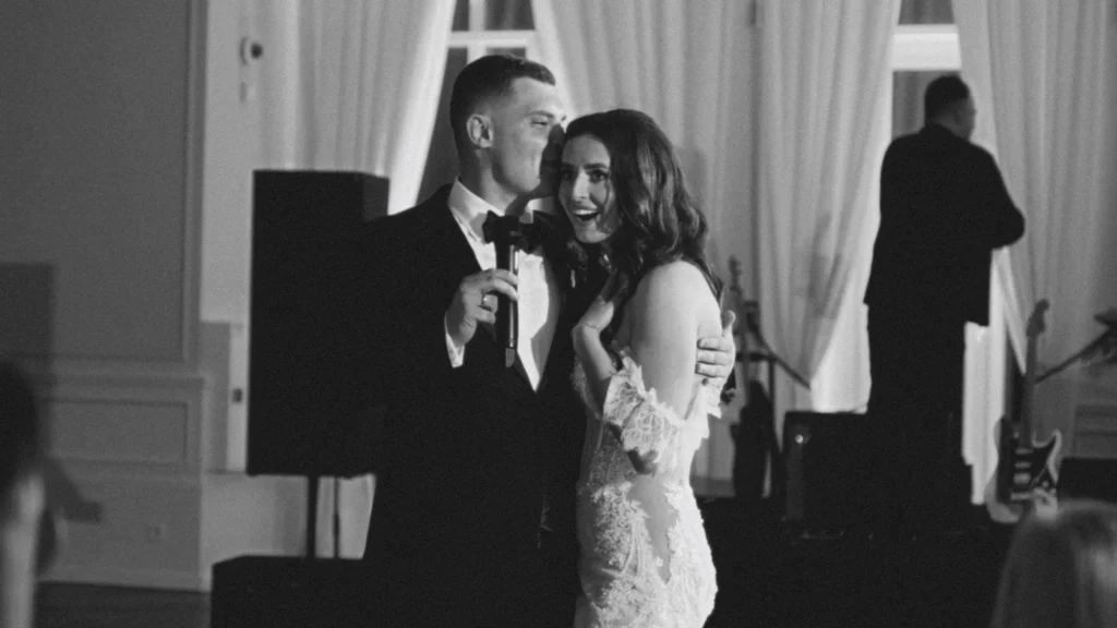 Newlyweds giving a toast on stage, the bride laughing in the groom's arms